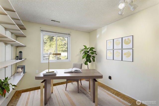 carpeted office space with a textured ceiling, visible vents, and baseboards