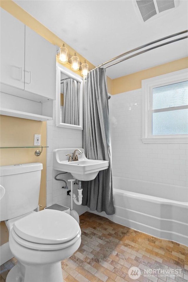 bathroom featuring toilet, shower / bath combination with curtain, and visible vents