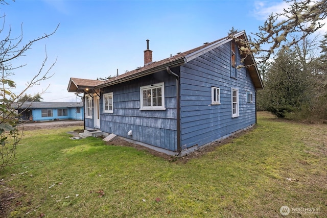 back of house with entry steps, a chimney, and a yard