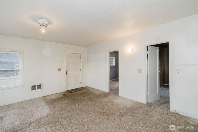 spare room featuring visible vents, a textured ceiling, and light colored carpet