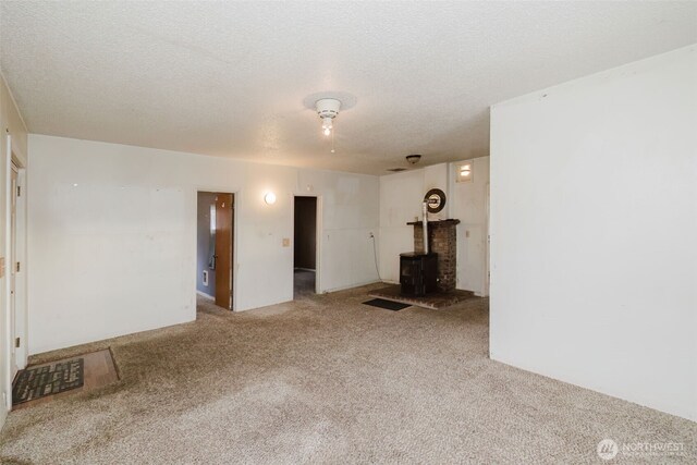 spare room with a wood stove, carpet floors, and a textured ceiling