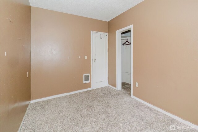 unfurnished bedroom with a textured ceiling, visible vents, baseboards, a spacious closet, and carpet