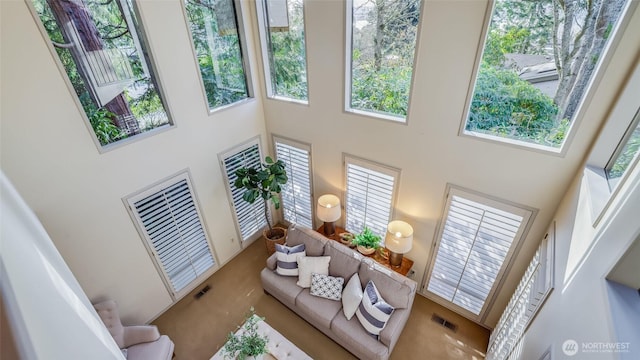 living room with a healthy amount of sunlight, visible vents, a towering ceiling, and stairway