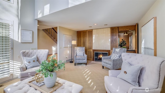 sitting room featuring carpet, stairs, and a glass covered fireplace