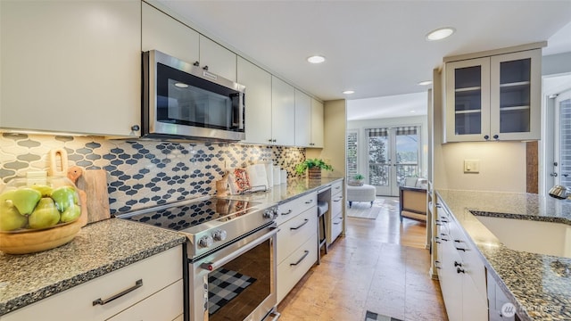 kitchen with stainless steel appliances, a sink, decorative backsplash, dark stone counters, and glass insert cabinets