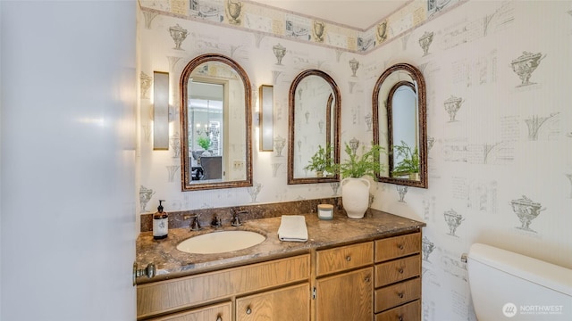 bathroom featuring vanity, toilet, and wallpapered walls