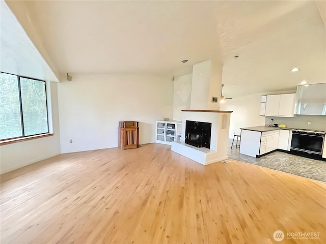 unfurnished living room with lofted ceiling, light wood-style flooring, and a multi sided fireplace