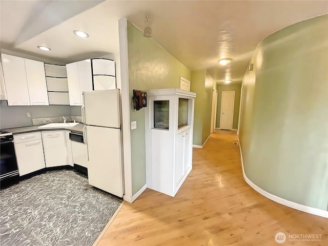 kitchen featuring stove, white cabinets, a sink, and freestanding refrigerator