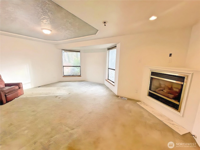 unfurnished living room featuring a textured ceiling, carpet, a fireplace with flush hearth, and visible vents