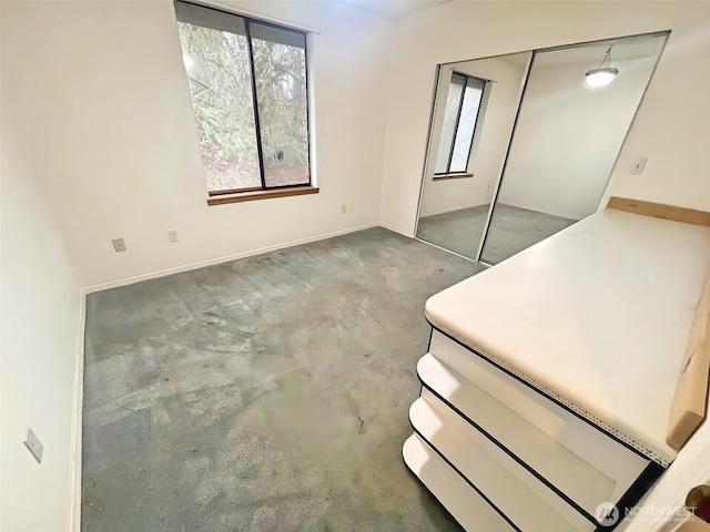 unfurnished bedroom with multiple windows, concrete floors, and baseboards