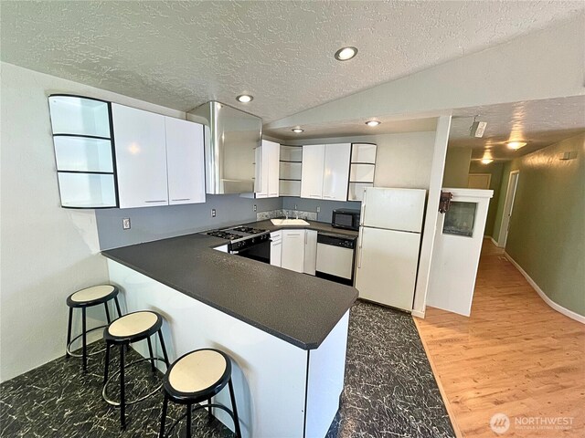 7116 Comanche Ln SW, Olympia, WA 98512 - kitchen featuring dark countertops, a textured ceiling, black appliances, a peninsula, and white cabinetry