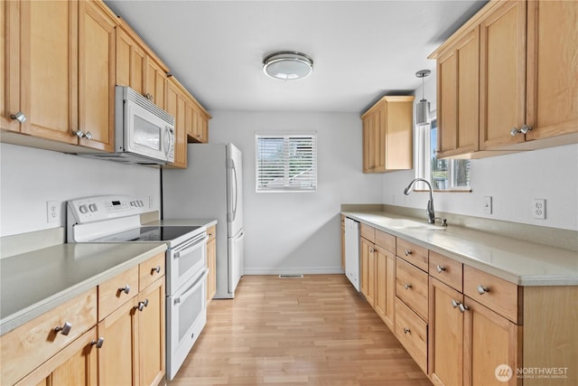 kitchen featuring white appliances, a sink, light countertops, hanging light fixtures, and a wealth of natural light