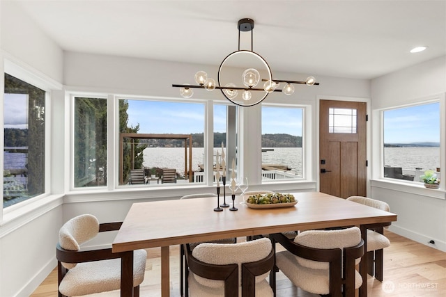 dining area with recessed lighting, a notable chandelier, a water view, baseboards, and light wood-style floors