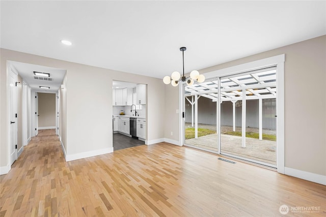 unfurnished dining area with a sink, light wood-style flooring, baseboards, and a notable chandelier