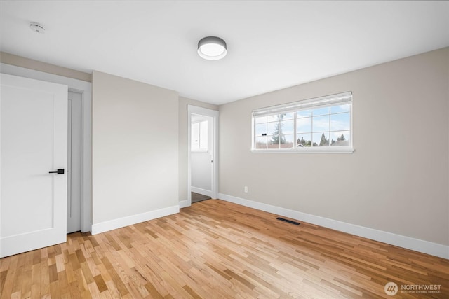 empty room with light wood-type flooring, visible vents, and baseboards