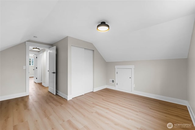 additional living space with light wood finished floors, visible vents, baseboards, and vaulted ceiling