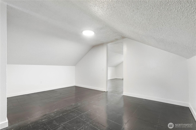 additional living space featuring baseboards, a textured ceiling, and vaulted ceiling