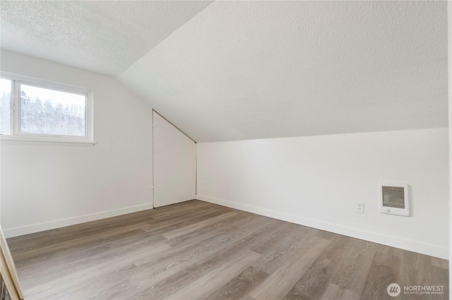 additional living space with visible vents, lofted ceiling, a textured ceiling, wood finished floors, and baseboards