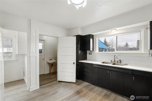 kitchen with light wood finished floors, a sink, backsplash, light countertops, and dark cabinets