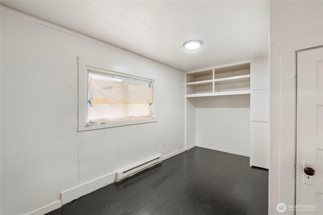 unfurnished room featuring a baseboard heating unit, baseboards, and dark wood-style flooring