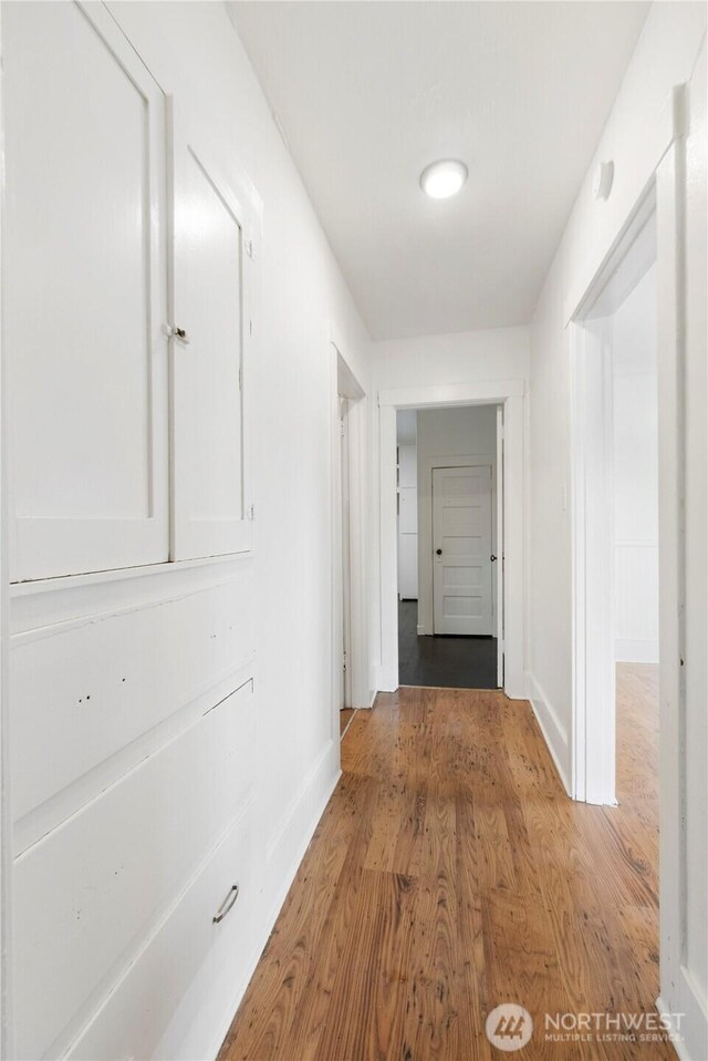 corridor with light wood-style flooring and baseboards