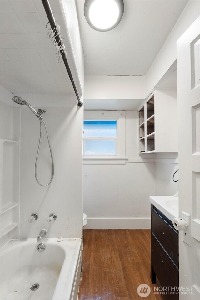 bathroom featuring vanity, wood finished floors, baseboards, bathing tub / shower combination, and toilet