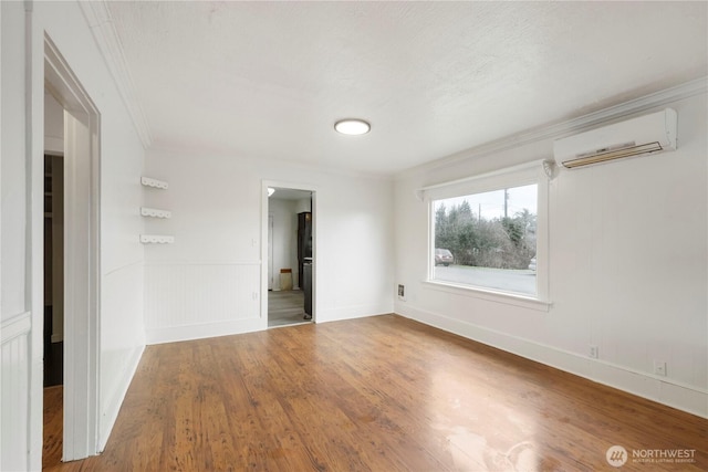 empty room featuring an AC wall unit, crown molding, wood finished floors, and wainscoting