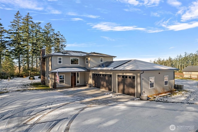 traditional home featuring a chimney, a porch, an attached garage, roof mounted solar panels, and driveway