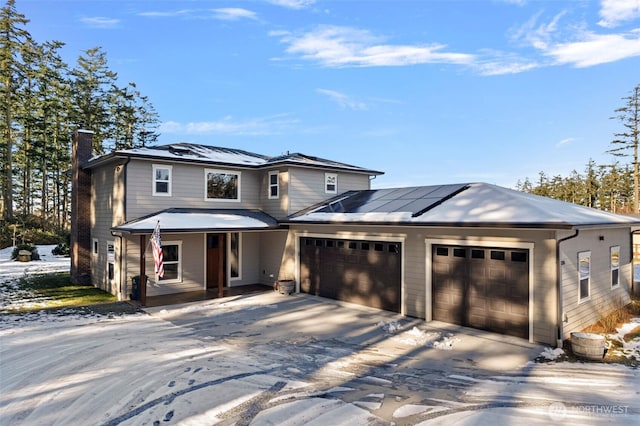 view of front facade featuring covered porch, a garage, driveway, roof mounted solar panels, and a chimney