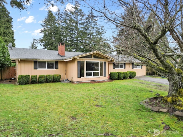 single story home featuring a shingled roof, a front lawn, fence, a chimney, and driveway