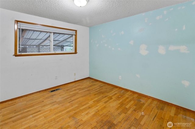 empty room featuring visible vents, a textured ceiling, baseboards, and hardwood / wood-style flooring