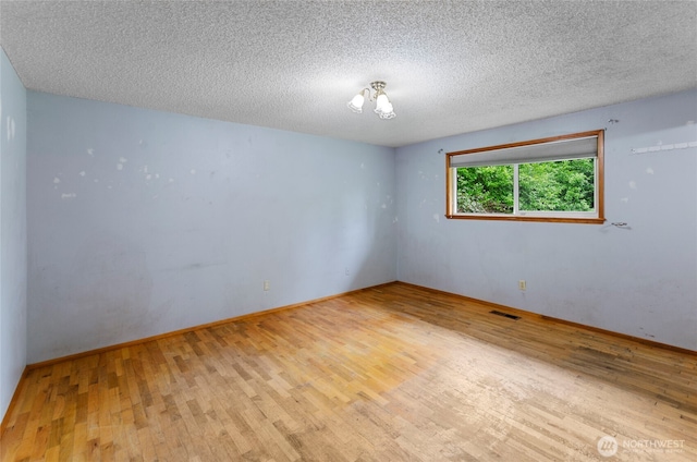 spare room with visible vents, a textured ceiling, baseboards, and wood finished floors