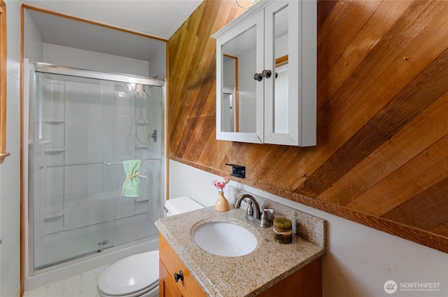 bathroom with vanity, toilet, wood walls, and a shower with door