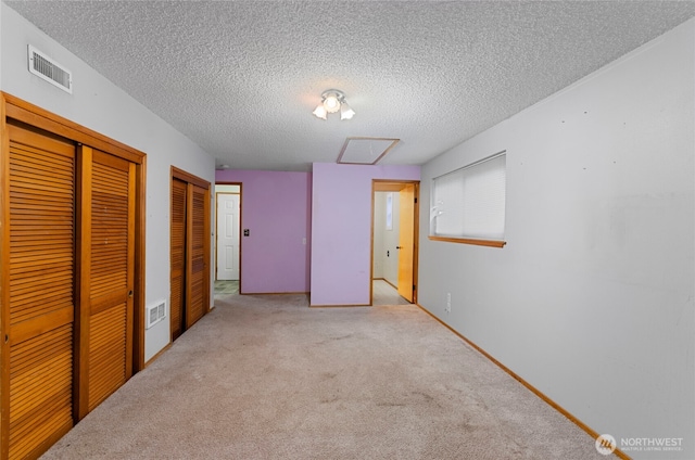 unfurnished bedroom featuring visible vents, a textured ceiling, multiple closets, and carpet floors