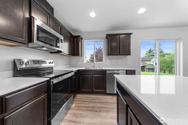 kitchen with dark brown cabinets, a sink, stainless steel appliances, light stone counters, and recessed lighting