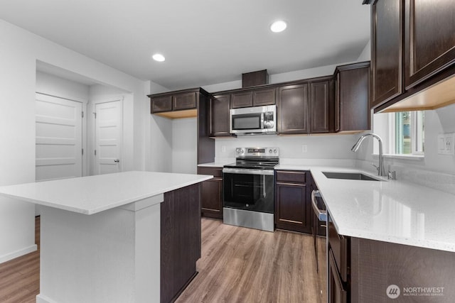 kitchen with light wood-type flooring, appliances with stainless steel finishes, dark brown cabinets, and a sink