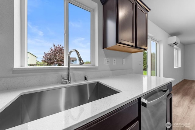 kitchen with dark brown cabinets, a sink, light stone countertops, dishwasher, and an AC wall unit
