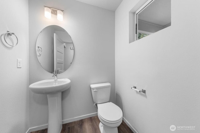 bathroom with toilet, wood finished floors, baseboards, and a sink
