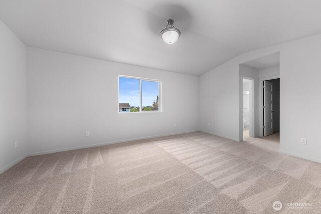 unfurnished room with lofted ceiling, baseboards, and light colored carpet