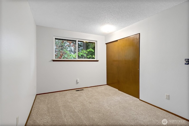 unfurnished bedroom with a textured ceiling, carpet floors, visible vents, baseboards, and a closet