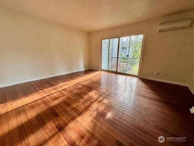 empty room with a textured ceiling, baseboards, wood finished floors, and a wall mounted AC