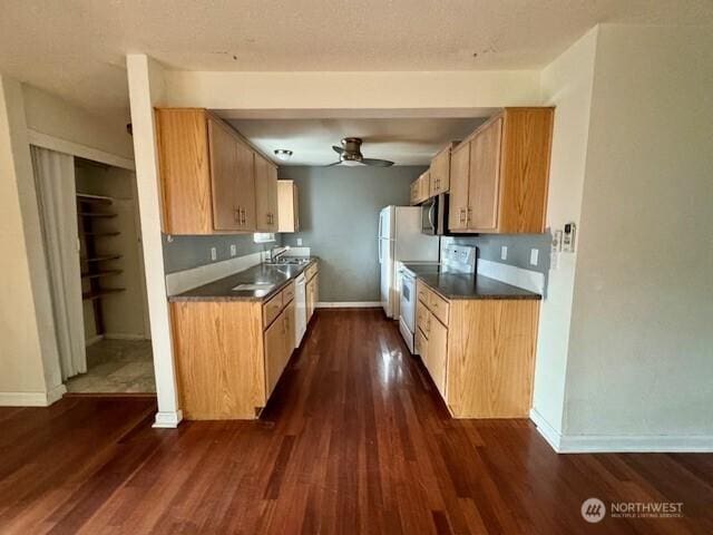 kitchen featuring white appliances, dark wood-type flooring, a ceiling fan, baseboards, and dark countertops