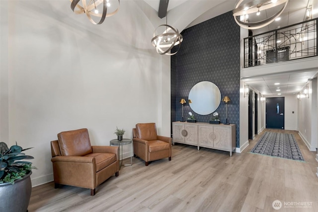 sitting room featuring a notable chandelier, an accent wall, wood finished floors, a towering ceiling, and baseboards