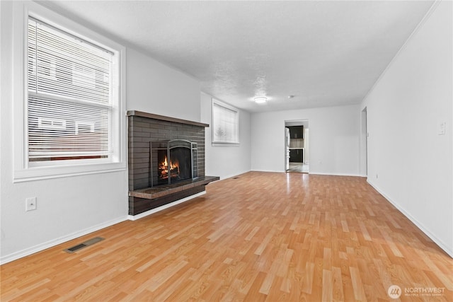 unfurnished living room with visible vents, baseboards, light wood-style flooring, a textured ceiling, and a fireplace