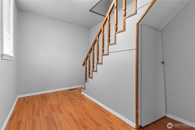 stairs with a textured ceiling, baseboards, and wood finished floors