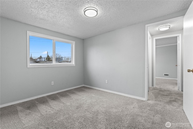 spare room featuring visible vents, light colored carpet, a textured ceiling, and baseboards