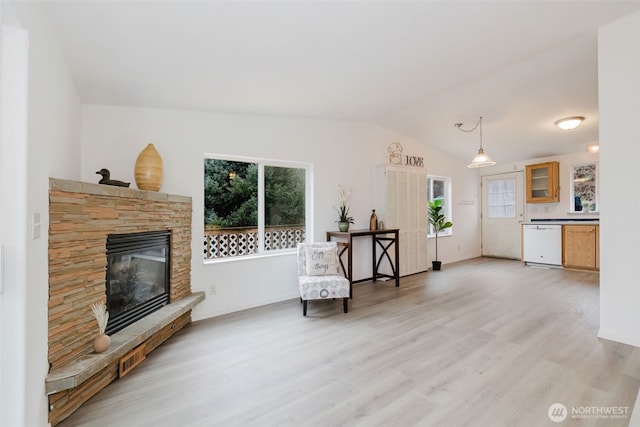 living area featuring light wood-type flooring, vaulted ceiling, a healthy amount of sunlight, and a fireplace