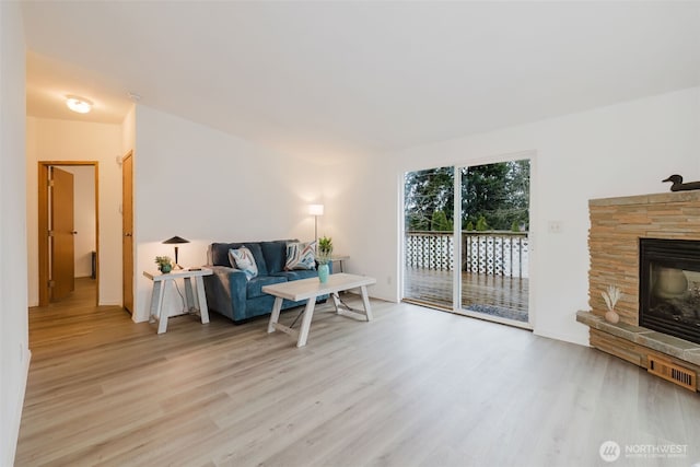 living room with a stone fireplace, light wood finished floors, and visible vents