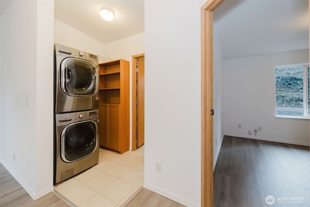 laundry room with stacked washing maching and dryer, baseboards, laundry area, and light wood-style floors