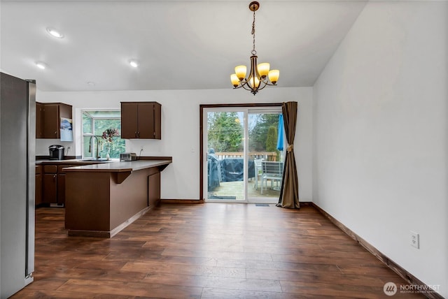 kitchen with dark wood finished floors, a breakfast bar, freestanding refrigerator, a peninsula, and a chandelier